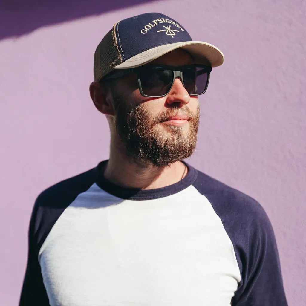 Man wearing a cap and sunglasses against a purple background