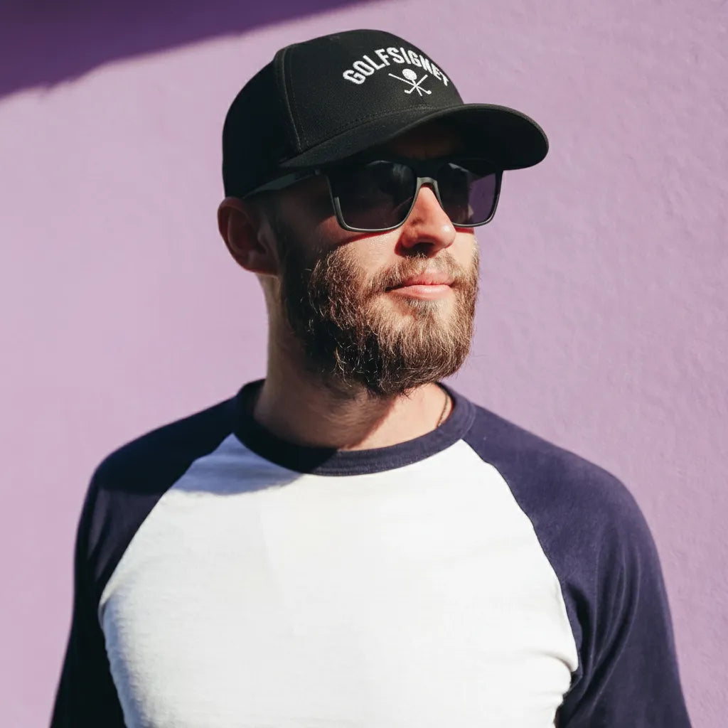 Man wearing a black cap with 'GolfSig' logo and sunglasses against a purple background
