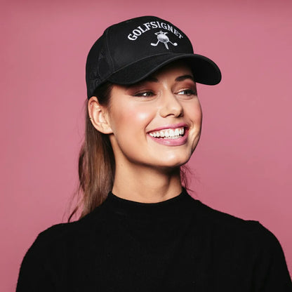Woman wearing a black cap with 'GOLFSIGNES' logo against a pink background
