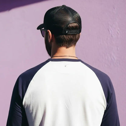 Person wearing a black cap and a two-tone shirt against a purple wall