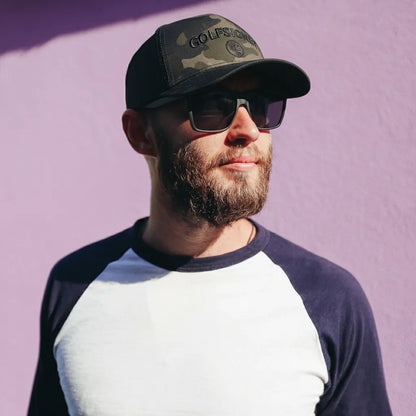 Man wearing a camouflage cap and sunglasses against a purple background