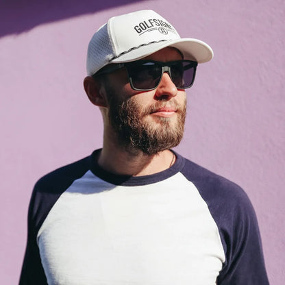 Man wearing a cap and sunglasses against a purple background